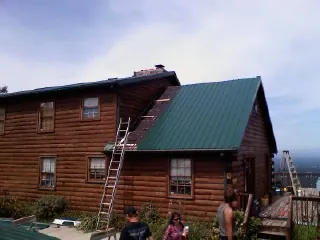 Green metal roof going on a two story log home with ladders set in Clayton